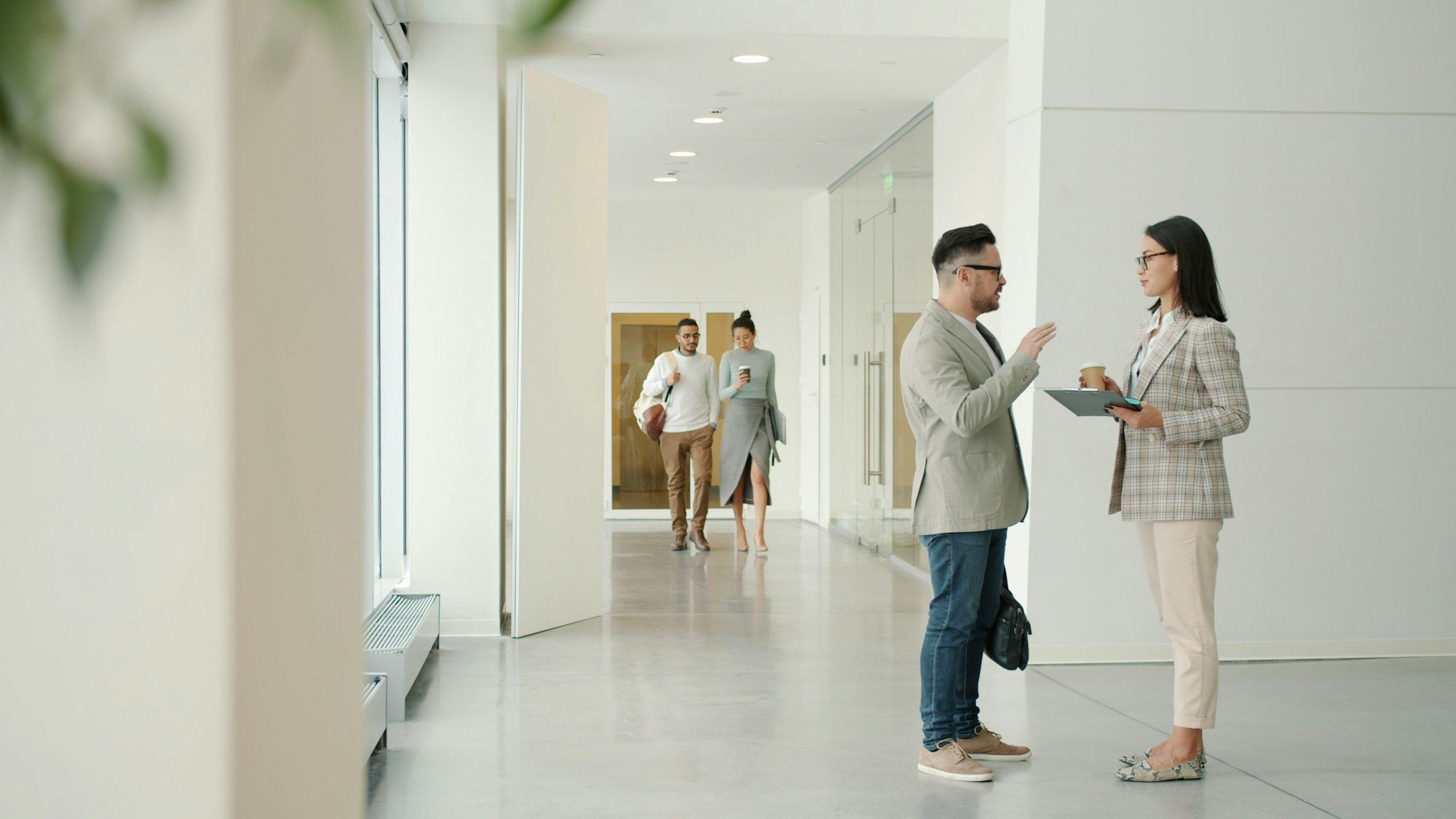 Two colleagues talking together while walking through a bright office hallway